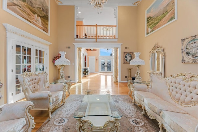 living room with a high ceiling, an inviting chandelier, light wood-type flooring, and french doors