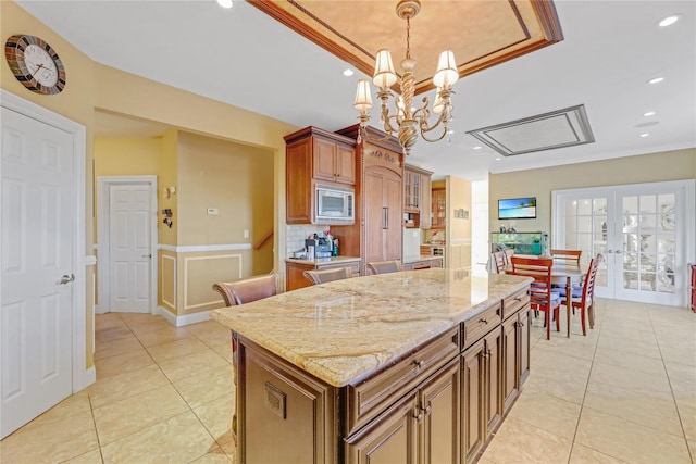 kitchen with light tile patterned floors, a center island, stainless steel microwave, decorative light fixtures, and french doors