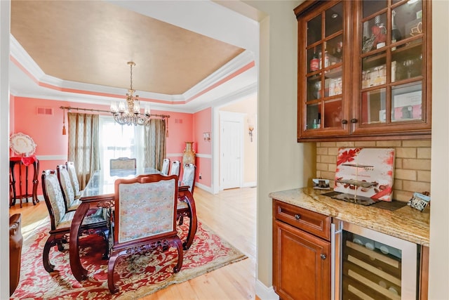 dining area featuring a raised ceiling, crown molding, wine cooler, and light hardwood / wood-style floors