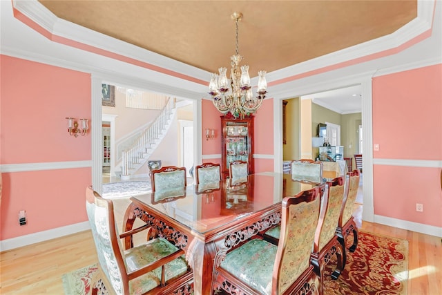 dining area with a chandelier, crown molding, a raised ceiling, and light hardwood / wood-style flooring