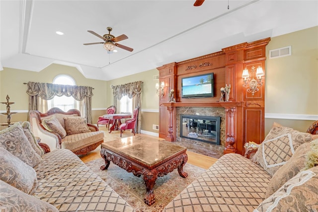 living room featuring lofted ceiling, a high end fireplace, ceiling fan, and light wood-type flooring