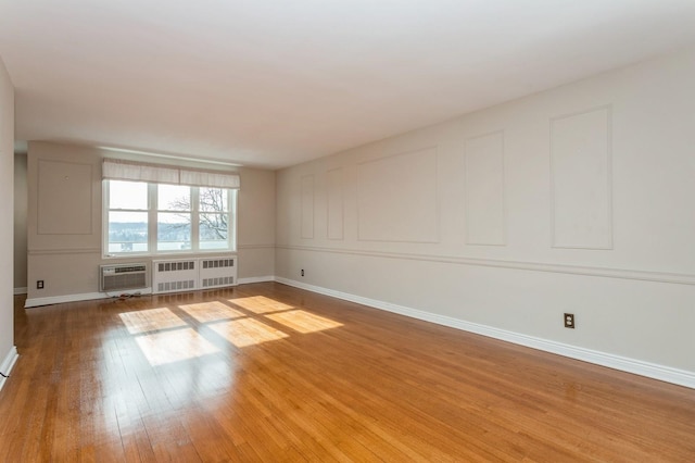 unfurnished room featuring radiator heating unit, hardwood / wood-style floors, and an AC wall unit