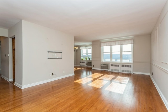 empty room featuring a wall mounted AC, radiator, hardwood / wood-style floors, and a notable chandelier