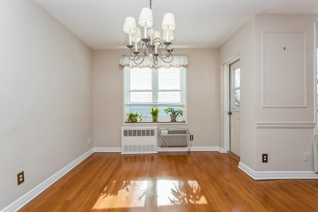 unfurnished dining area featuring radiator, a wall mounted air conditioner, an inviting chandelier, and light wood-type flooring