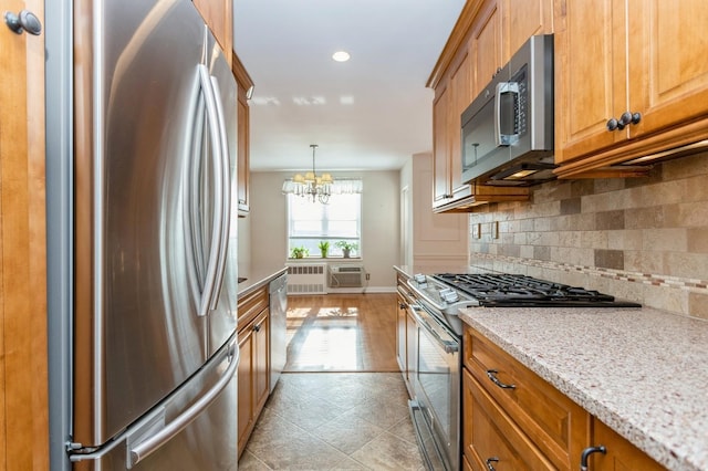 kitchen featuring appliances with stainless steel finishes, a wall mounted AC, a notable chandelier, light stone countertops, and decorative backsplash