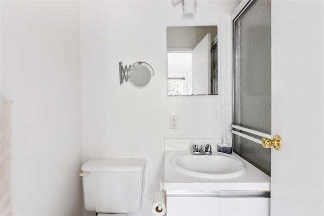 bathroom featuring a shower with door, vanity, and toilet