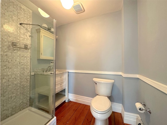 bathroom with wood-type flooring, tiled shower, vanity, and toilet