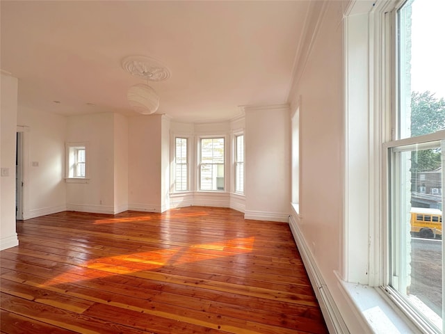 unfurnished room featuring dark wood-type flooring, ornamental molding, and a healthy amount of sunlight