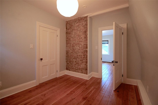 spare room featuring wood-type flooring and brick wall