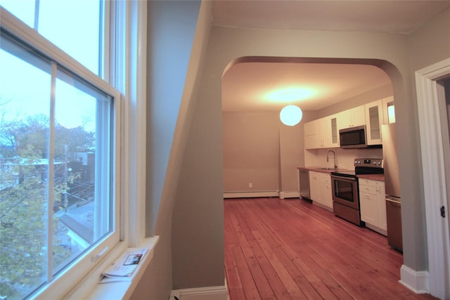 kitchen featuring sink, light wood-type flooring, a baseboard radiator, stainless steel appliances, and white cabinets