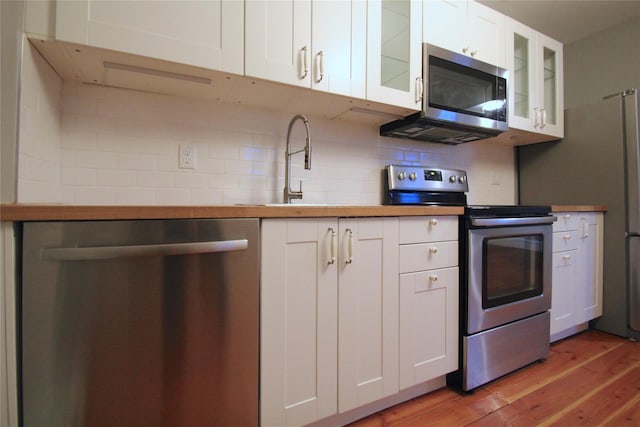 kitchen with tasteful backsplash, stainless steel appliances, light hardwood / wood-style floors, and white cabinets