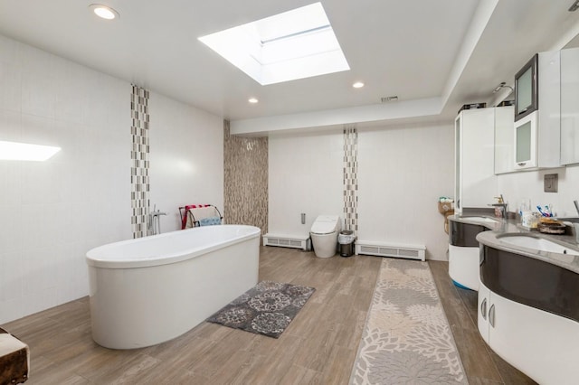 bathroom featuring hardwood / wood-style flooring, tile walls, a skylight, vanity, and a bath