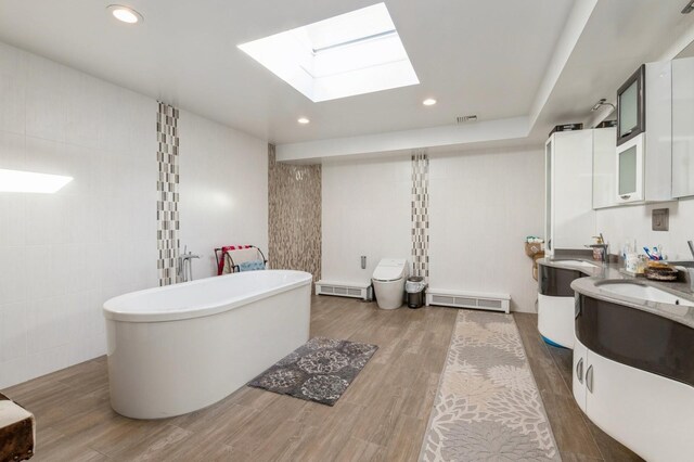 bathroom featuring wood-type flooring, a skylight, tile walls, vanity, and a washtub