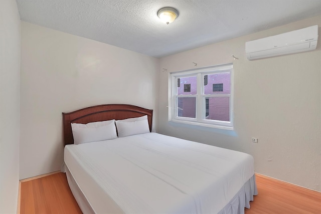 bedroom with a wall mounted AC, light hardwood / wood-style floors, and a textured ceiling