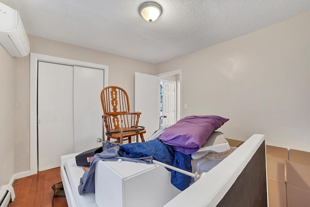 bedroom featuring baseboard heating, an AC wall unit, a textured ceiling, dark hardwood / wood-style flooring, and a closet