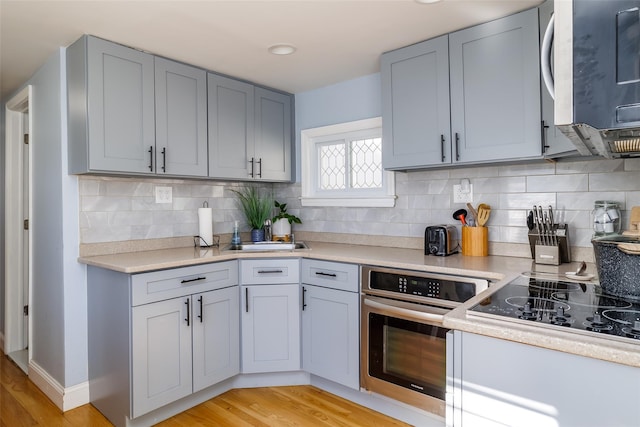 kitchen with sink, gray cabinets, stainless steel appliances, tasteful backsplash, and light hardwood / wood-style floors