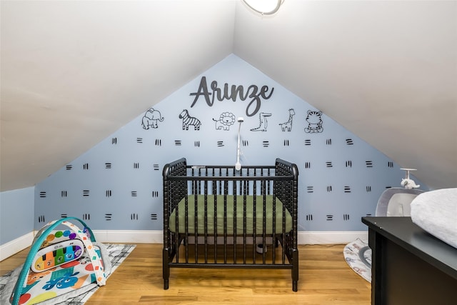 bedroom featuring lofted ceiling, hardwood / wood-style flooring, and a nursery area