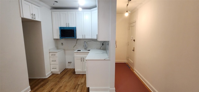 kitchen featuring sink, crown molding, wood-type flooring, decorative backsplash, and white cabinets