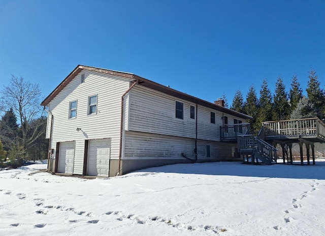 snow covered rear of property featuring a wooden deck and a garage