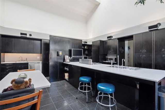 kitchen featuring a kitchen breakfast bar, dishwasher, sink, and a high ceiling