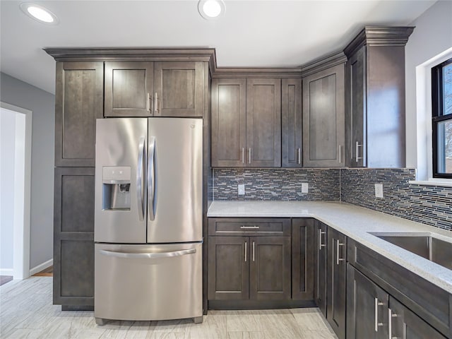 kitchen featuring sink, stainless steel fridge, backsplash, light stone counters, and dark brown cabinetry