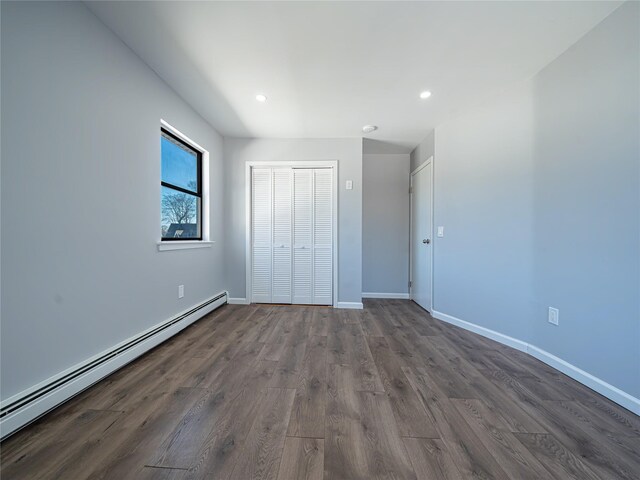 unfurnished bedroom with a baseboard radiator, dark hardwood / wood-style floors, and a closet