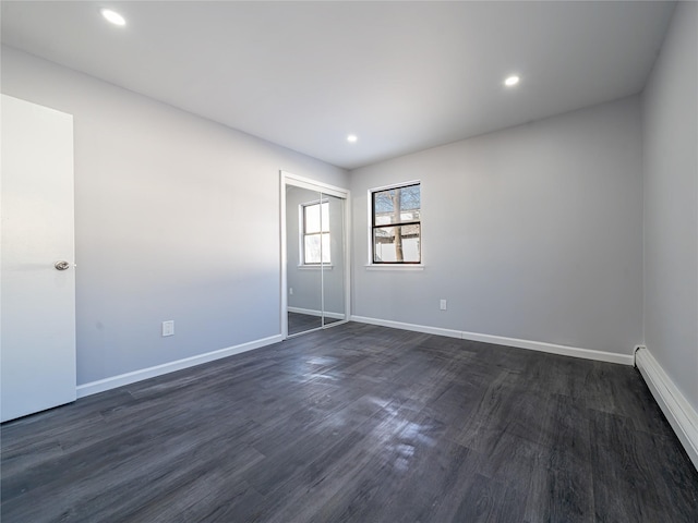 empty room featuring baseboard heating and dark hardwood / wood-style flooring