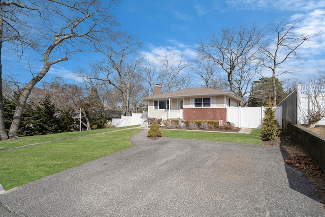 view of front of property featuring brick siding, a chimney, aphalt driveway, fence, and a front yard