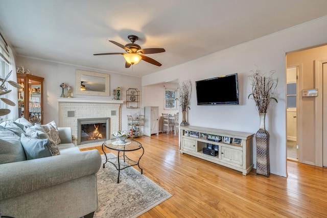 living area with a fireplace, light wood finished floors, ornamental molding, a ceiling fan, and baseboards