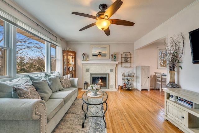 living room featuring ornamental molding, a brick fireplace, a ceiling fan, and light wood-style floors