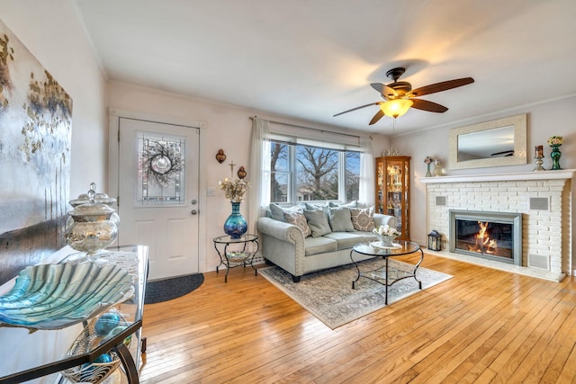 living area with light wood-style flooring, a fireplace, a ceiling fan, and crown molding