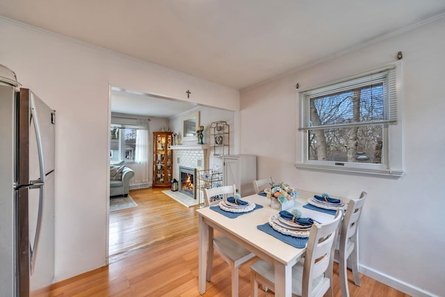 dining space with a brick fireplace, light wood-style flooring, baseboards, and crown molding