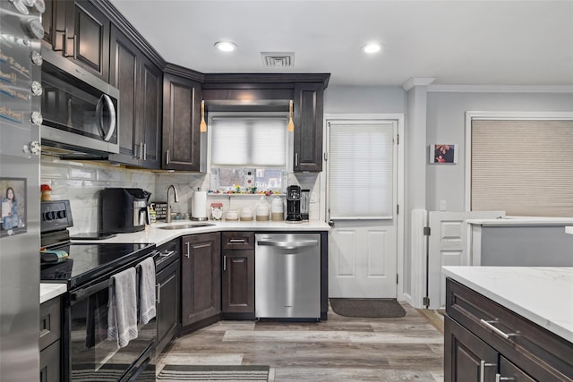 kitchen with appliances with stainless steel finishes, tasteful backsplash, sink, ornamental molding, and light hardwood / wood-style flooring