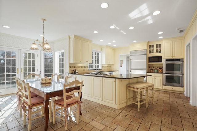 kitchen featuring hanging light fixtures, built in appliances, a kitchen island, decorative backsplash, and cream cabinetry