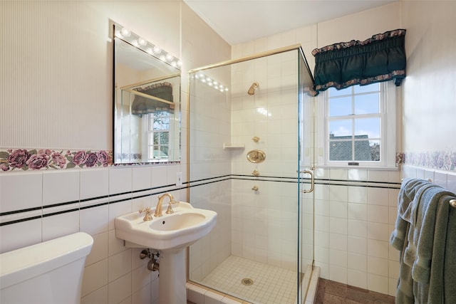 bathroom with toilet, tile walls, and a shower with shower door