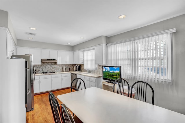 kitchen with white cabinetry, backsplash, fridge, stainless steel dishwasher, and light hardwood / wood-style floors