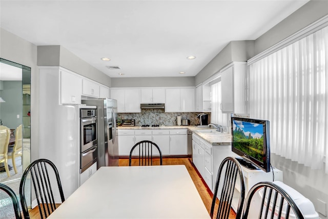 kitchen with sink, stainless steel appliances, light hardwood / wood-style floors, white cabinets, and decorative backsplash