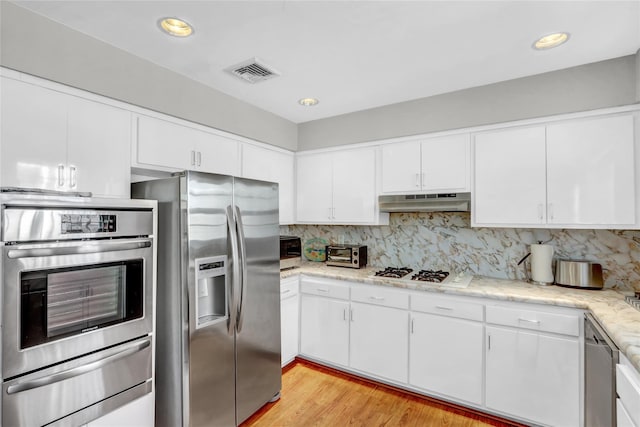 kitchen with appliances with stainless steel finishes, white cabinetry, backsplash, light stone counters, and light wood-type flooring