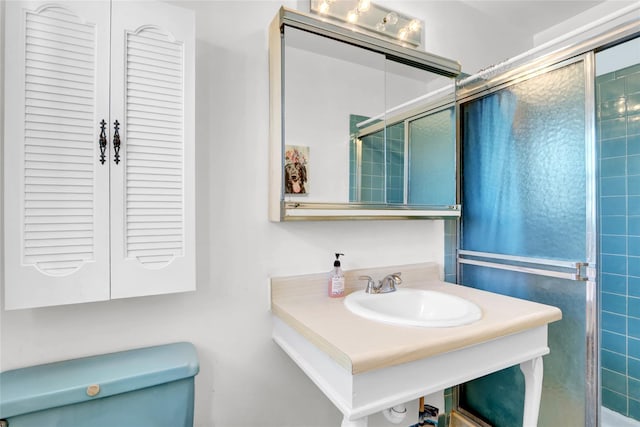 bathroom featuring a shower with shower door, sink, and toilet