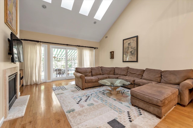 living room with a skylight, a high end fireplace, high vaulted ceiling, and light wood-type flooring