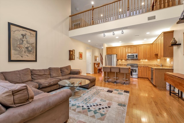 living room with a towering ceiling, sink, and light hardwood / wood-style floors