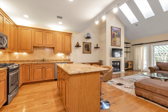 kitchen featuring a center island, a kitchen breakfast bar, stainless steel appliances, light stone countertops, and light hardwood / wood-style floors