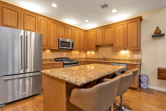 kitchen featuring a kitchen island, appliances with stainless steel finishes, light stone counters, and a kitchen breakfast bar