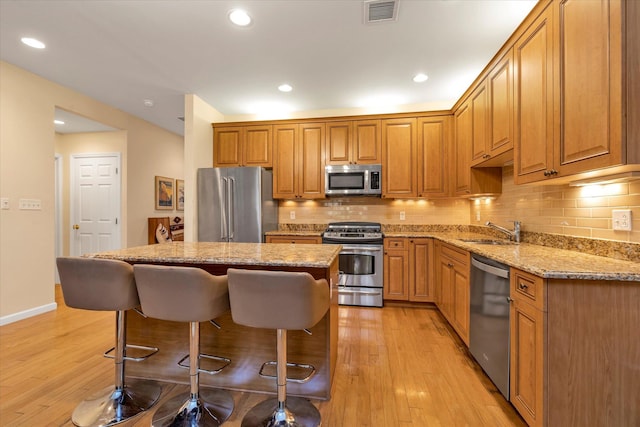 kitchen featuring sink, stainless steel appliances, tasteful backsplash, light stone countertops, and light wood-type flooring