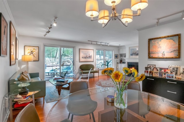 dining space featuring a notable chandelier, crown molding, wood-type flooring, and rail lighting