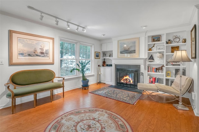 sitting room with a tiled fireplace, built in features, ornamental molding, and light wood-type flooring