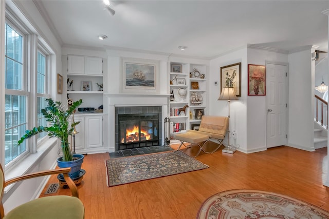 living room with crown molding, built in features, wood-type flooring, and a tile fireplace