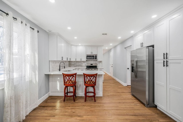 kitchen with a kitchen bar, white cabinetry, kitchen peninsula, stainless steel appliances, and light hardwood / wood-style floors