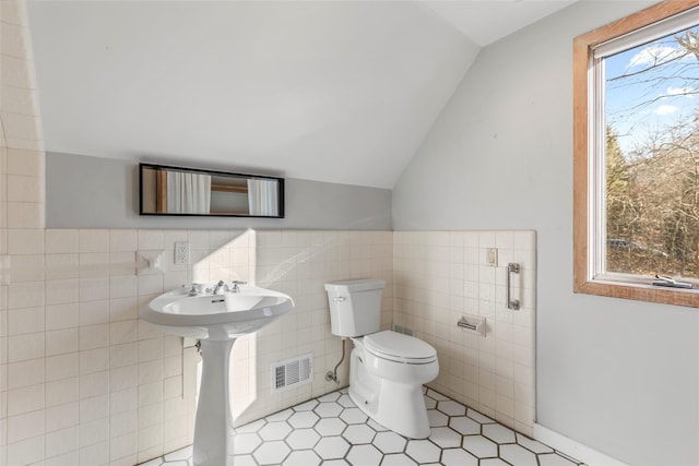 bathroom with tile patterned flooring, vaulted ceiling, tile walls, and toilet