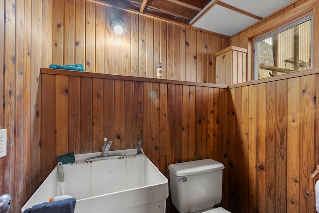 bathroom featuring sink, wooden walls, and toilet